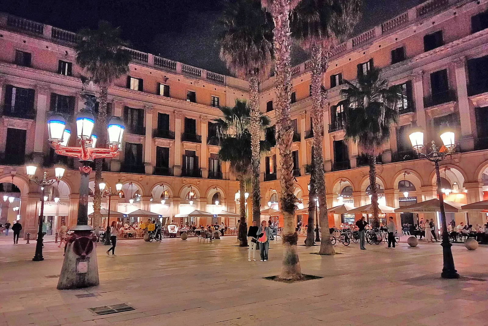 One of the street lamps Antoni Gaudí designed for Plaça Reial, lit at night, with palm trees and arcaded buildings behind