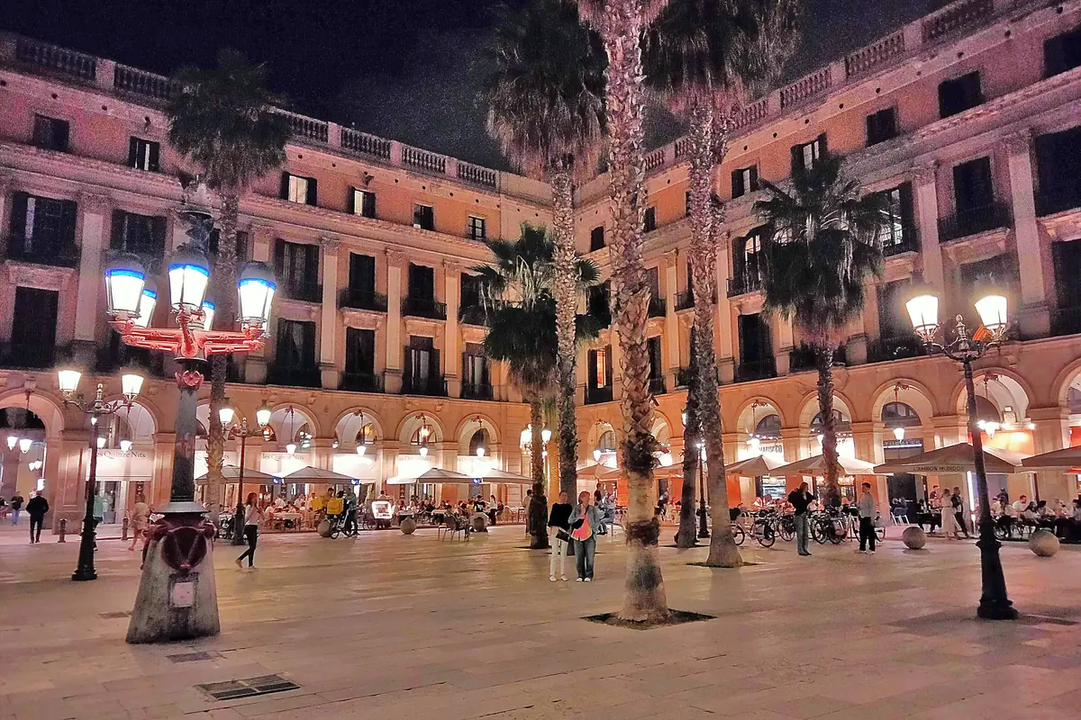 One of the street lamps Antoni Gaudí designed for Plaça Reial, lit at night, with palm trees and arcaded buildings behind